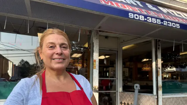 Jacqueline Tejera, vistiendo una camiseta gris y un delantal rojo, con el local de la Pizzer&iacute;a Montevideo detr&aacute;s.